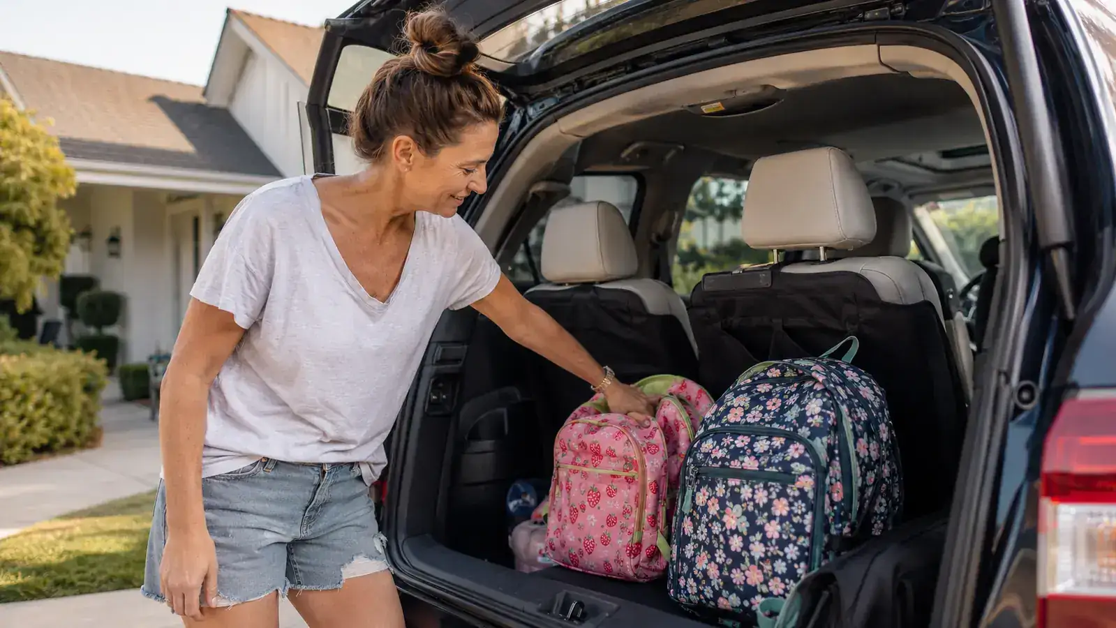 Mom and two kids loading into an SUV for a road trip, phones and gear visible in the back seat