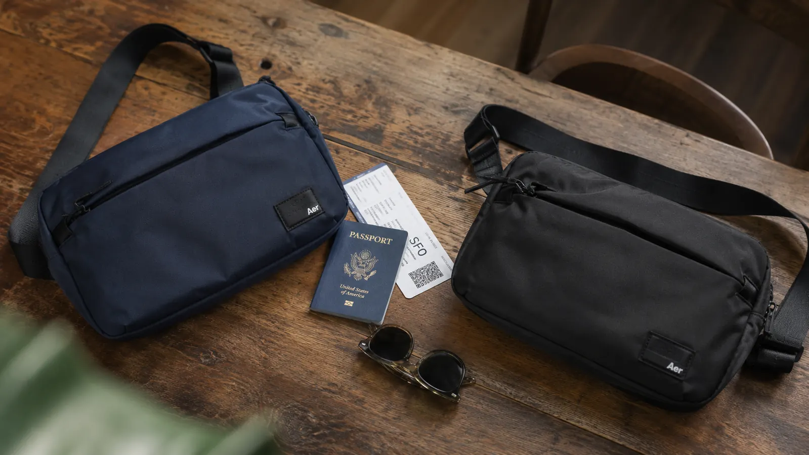 Two crossbody anti-theft bags side by side on a wooden table, one budget and one premium, with a passport and sunglasses nearby